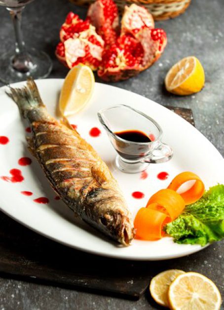 side-view-baked-sea-bass-served-with-lemonnd-narsharab-sauce-white-platter-black_140725-11837